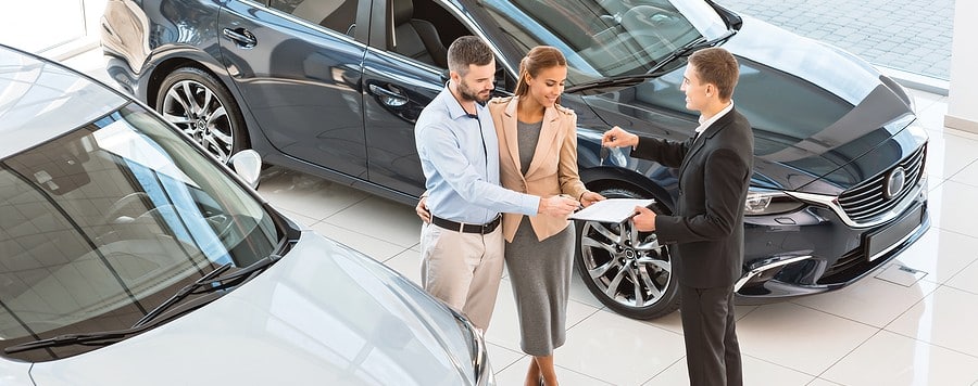 Top view photo of young male consultant and buyers signing contract for new car in auto showroom