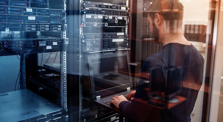 An IT professional with a laptop is in a network server room.
