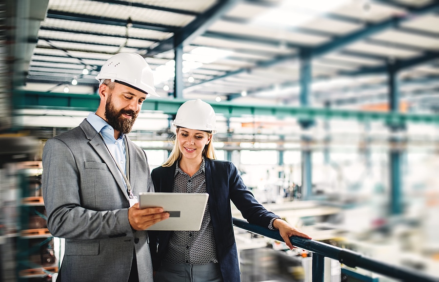 A portrait of two professional engineers looking at a tablet in an industrial manufacturing facility.